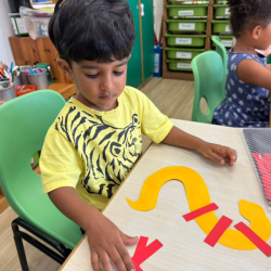 Aarav focusing on pasting paper pieces on his snake to create a pattern .