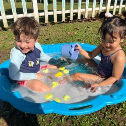 Alex and Celen scoop rubber ducks in the tub on a sunny day.