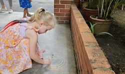 Regan enjoying drawing a rainbow using chalk.