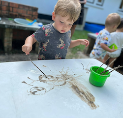 Leo enjoying painting with mud using a stick!