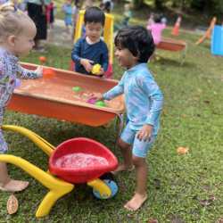 Eleanor and Aarav working together in putting water in the wheelbarrow.